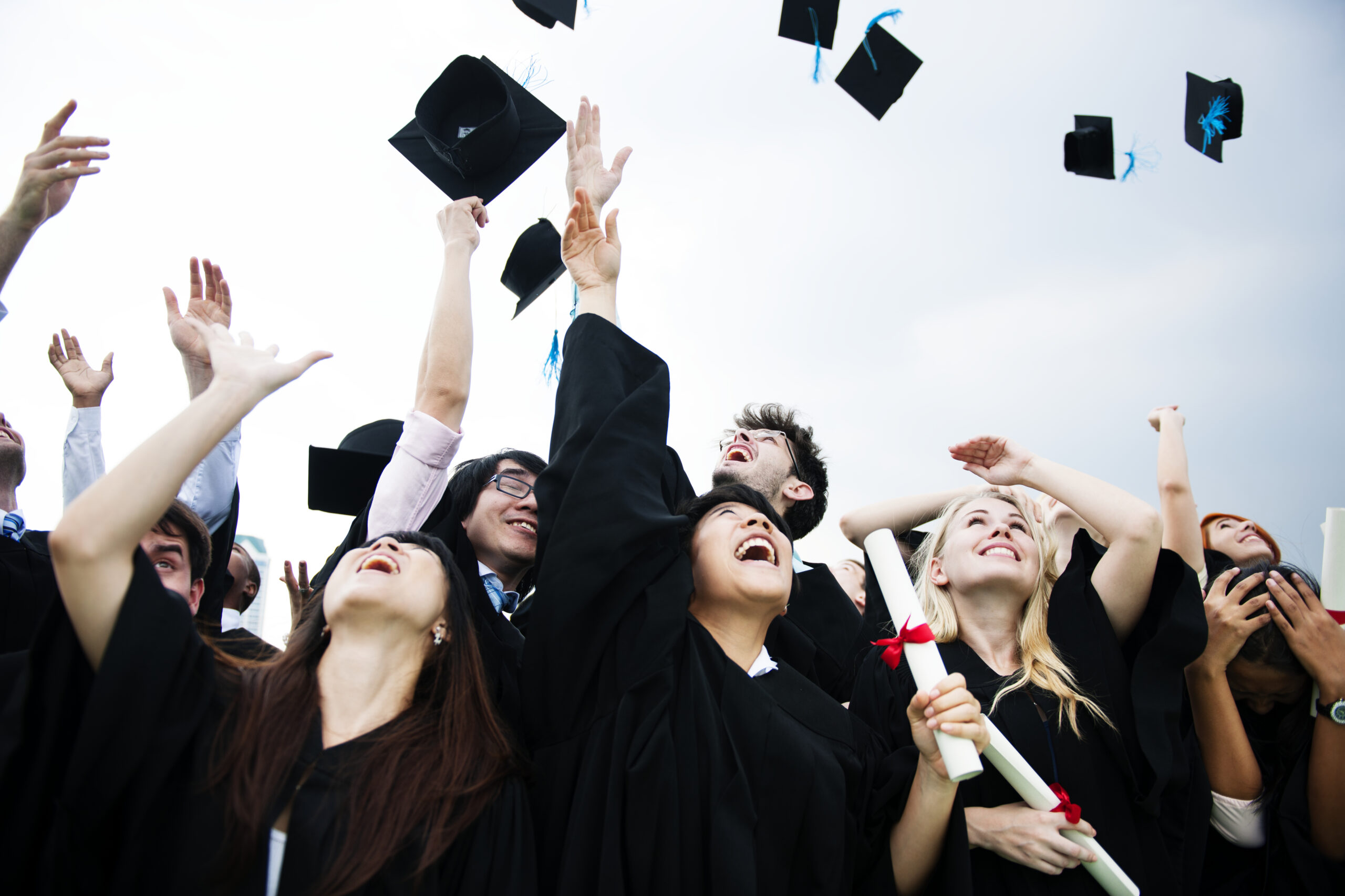 group diverse grads throwing caps up sky scaled 1